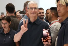 Tim Cook gestures to the crowd while holding an iPhone during a public Apple event, underscoring the product-driven leadership era he is set to transition away from later this year.