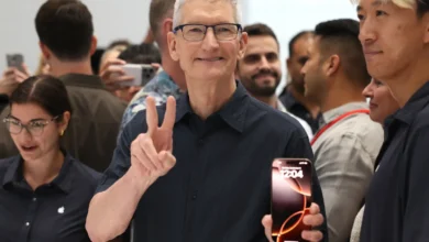 Tim Cook gestures to the crowd while holding an iPhone during a public Apple event, underscoring the product-driven leadership era he is set to transition away from later this year.