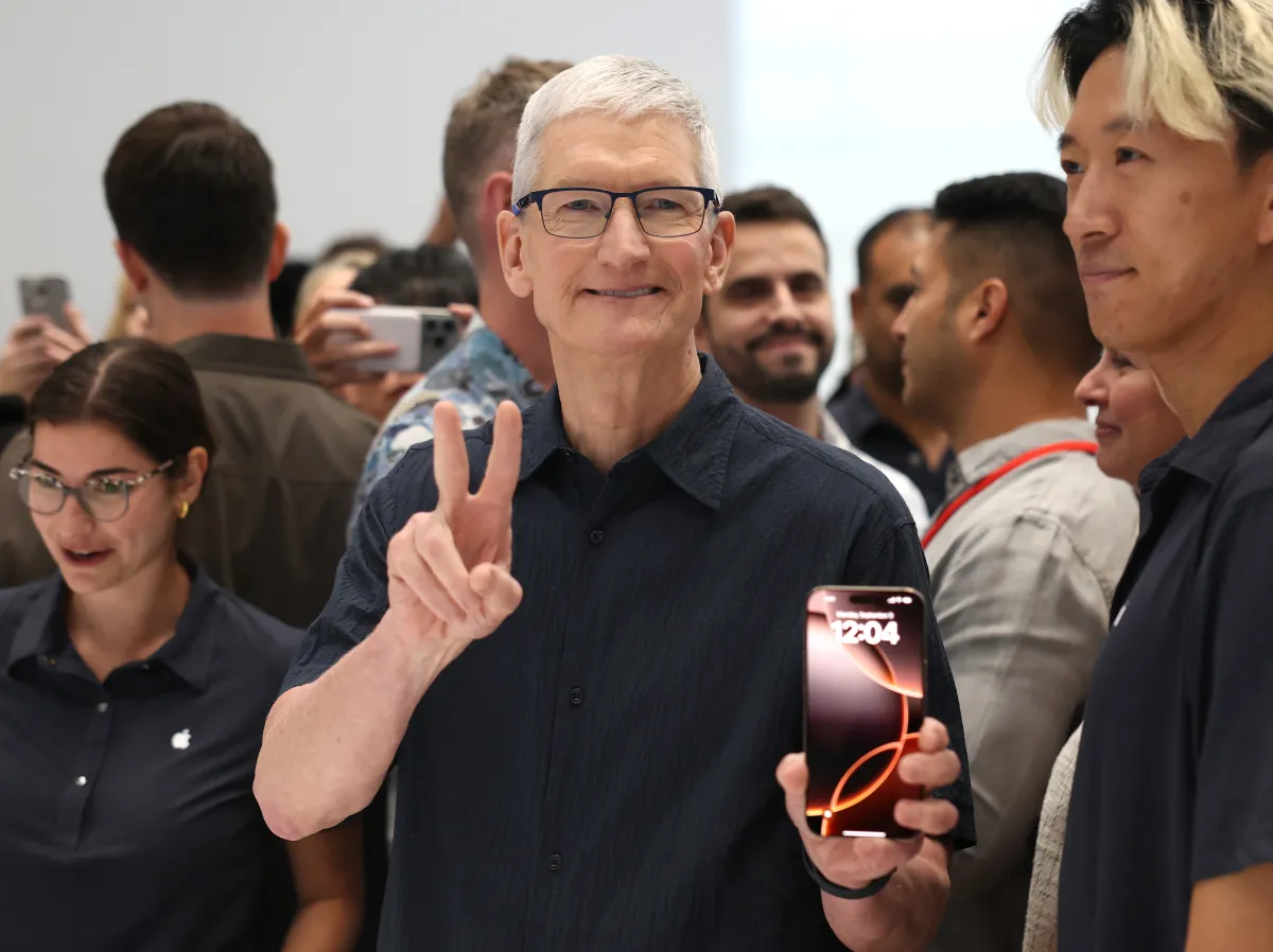 Tim Cook gestures to the crowd while holding an iPhone during a public Apple event, underscoring the product-driven leadership era he is set to transition away from later this year.