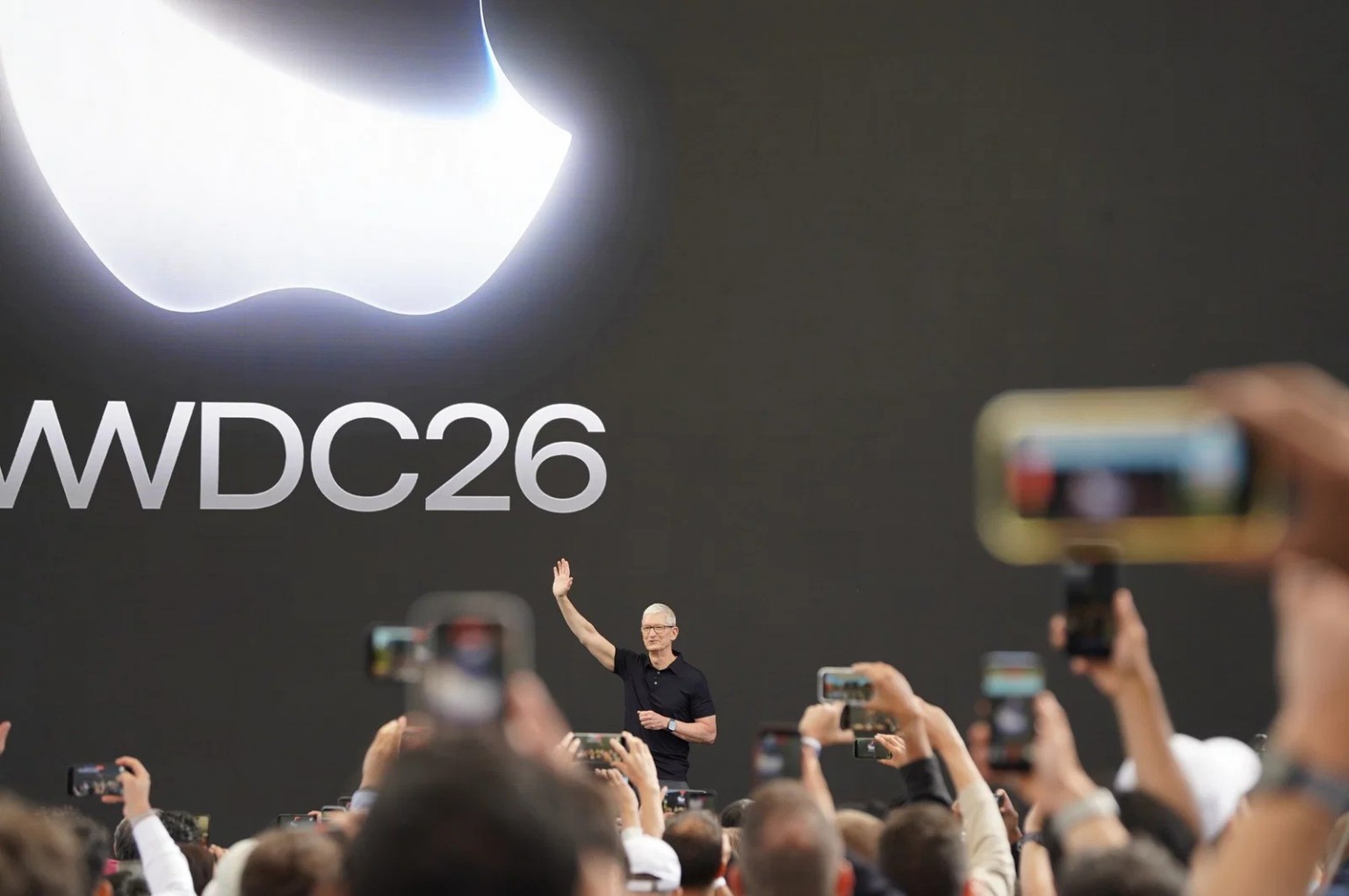 Tim Cook waves to attendees beneath a large WWDC 2026 display during Apple's annual developer conference.