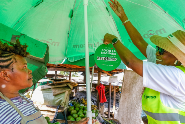Safaricom representative helps a Kenyan woman entrepreneur set up Pochi la Biashara at a market stall.