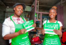 Two Kenyan women entrepreneurs holding Pochi la Biashara merchant signs inside a small retail shop.