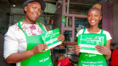 Two Kenyan women entrepreneurs holding Pochi la Biashara merchant signs inside a small retail shop.