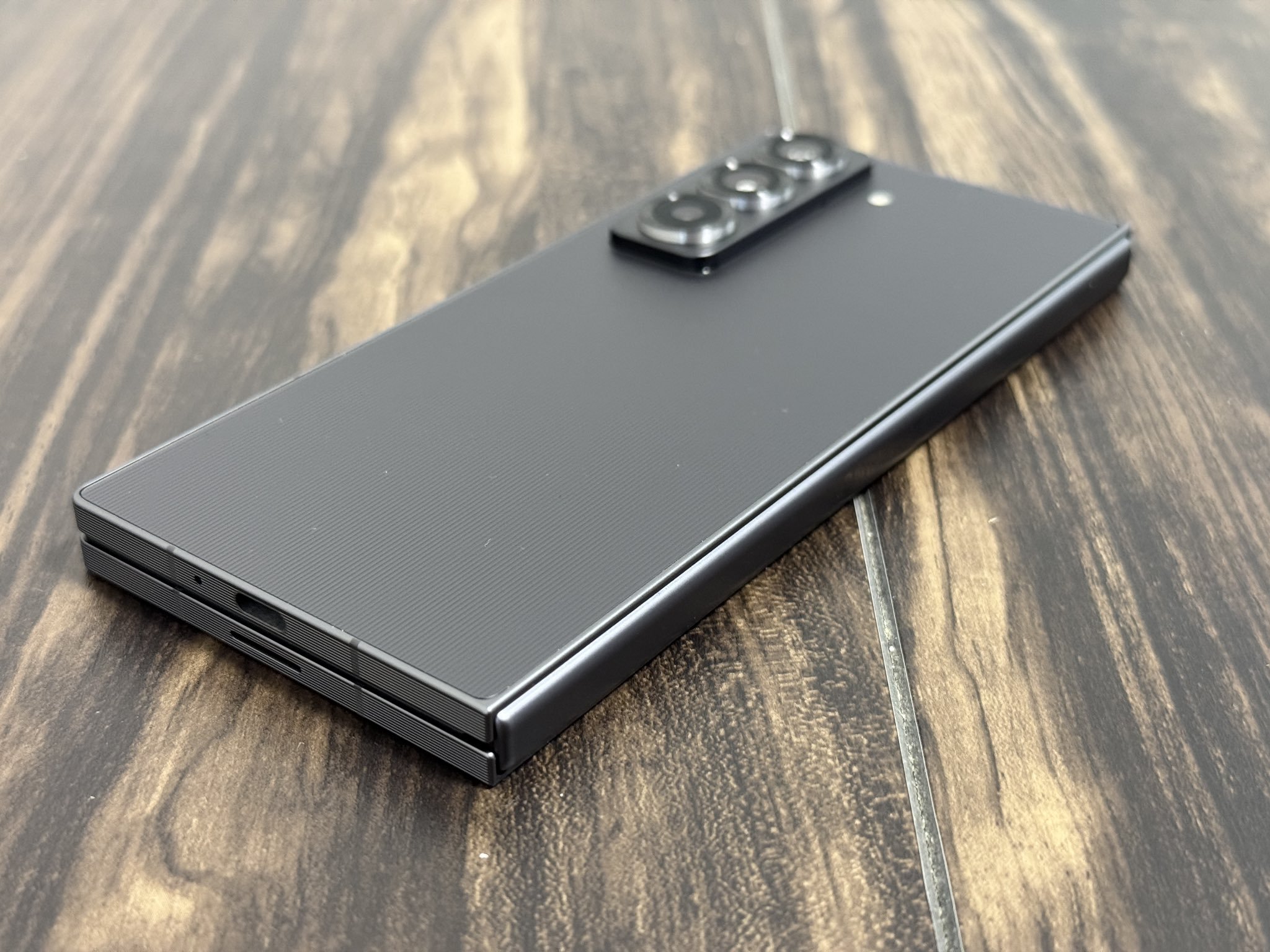 Samsung Galaxy Z Fold8 folded closed on a wooden table, showing its slim profile and rear camera module.