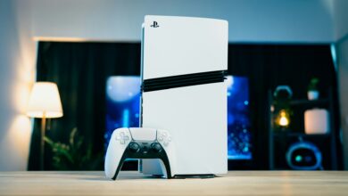 A white PlayStation 5 console standing beside a DualSense controller on a table in a modern gaming setup.