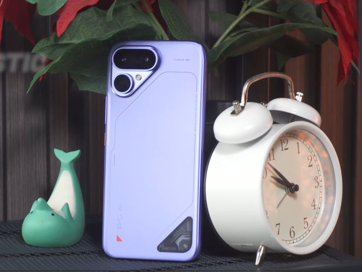 TECNO POVA Curve 2 5G in Mystic Purple showing its slim rear design and dual-camera module beside a white alarm clock.