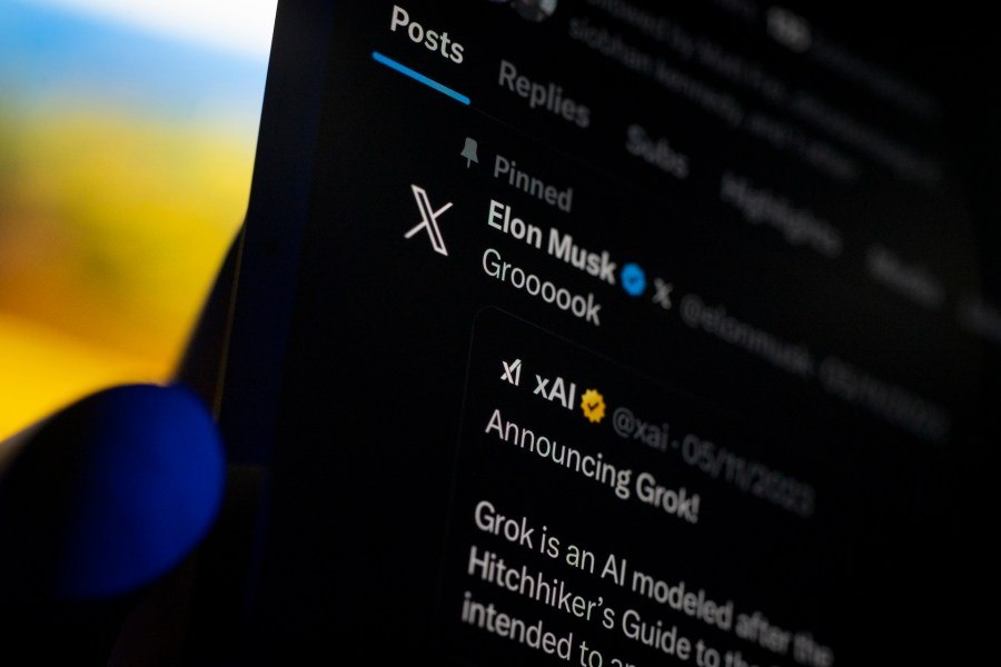 A smartphone displaying the X app with Elon Musk's profile and a Grok announcement on screen.