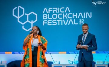 Speakers on stage at the Africa Blockchain Festival in Kigali with the event logo displayed on a large blue backdrop.