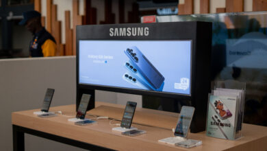Samsung Galaxy S26 smartphones on a wooden retail display stand beneath a backlit Samsung Galaxy S26 Series banner featuring Galaxy AI.