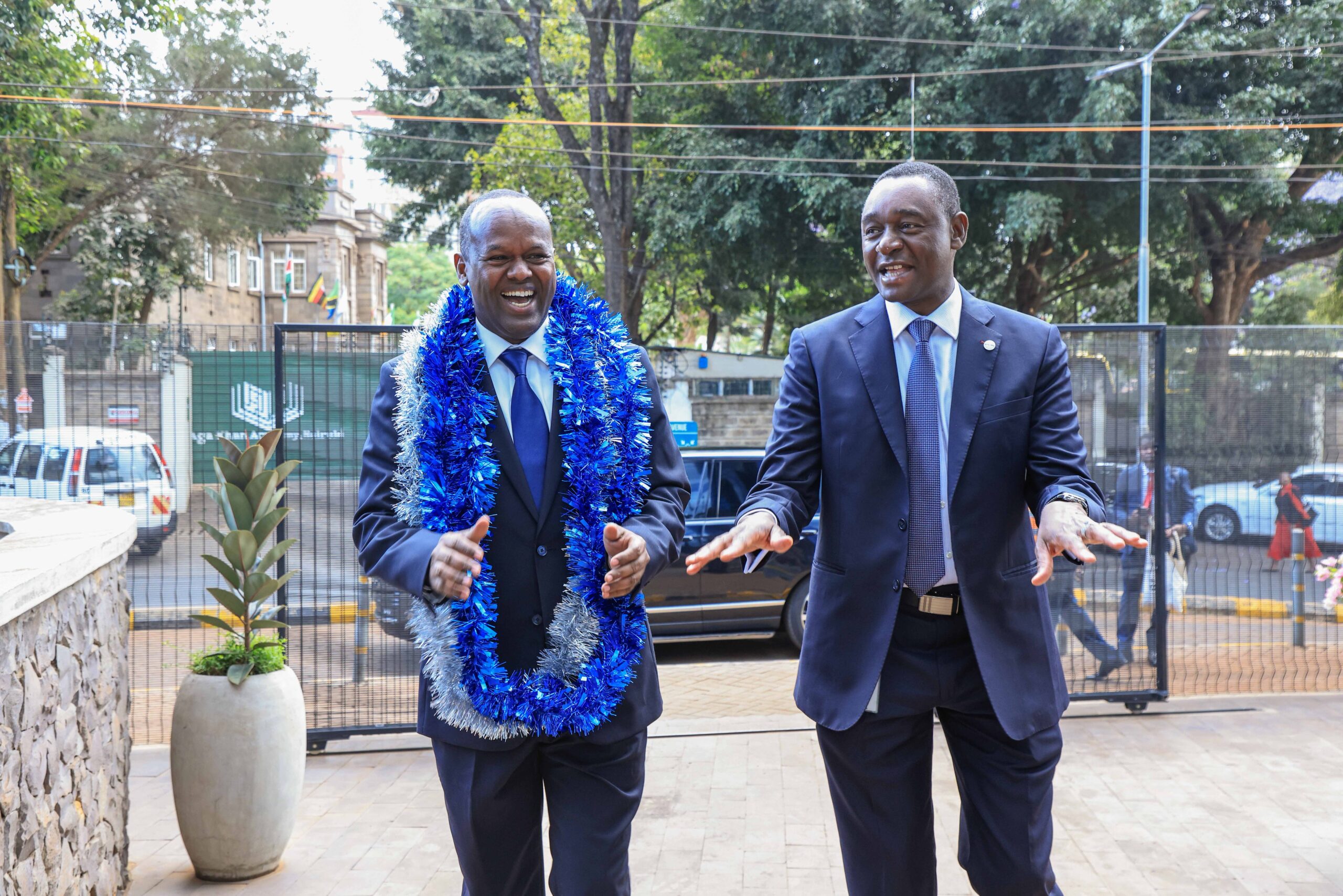 Newly appointed I&M Bank Kenya CEO Abdi Mohamed wearing a blue garland alongside Regional CEO Kihara Maina outside the bank's premises.
